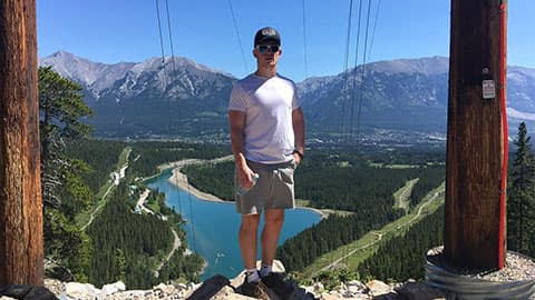 Harry standing in the sunshine on top of a mountain with mountains and blue sky in the background in Canada.